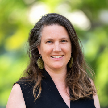 Woman with long hair smiling outdoors with green blurred background